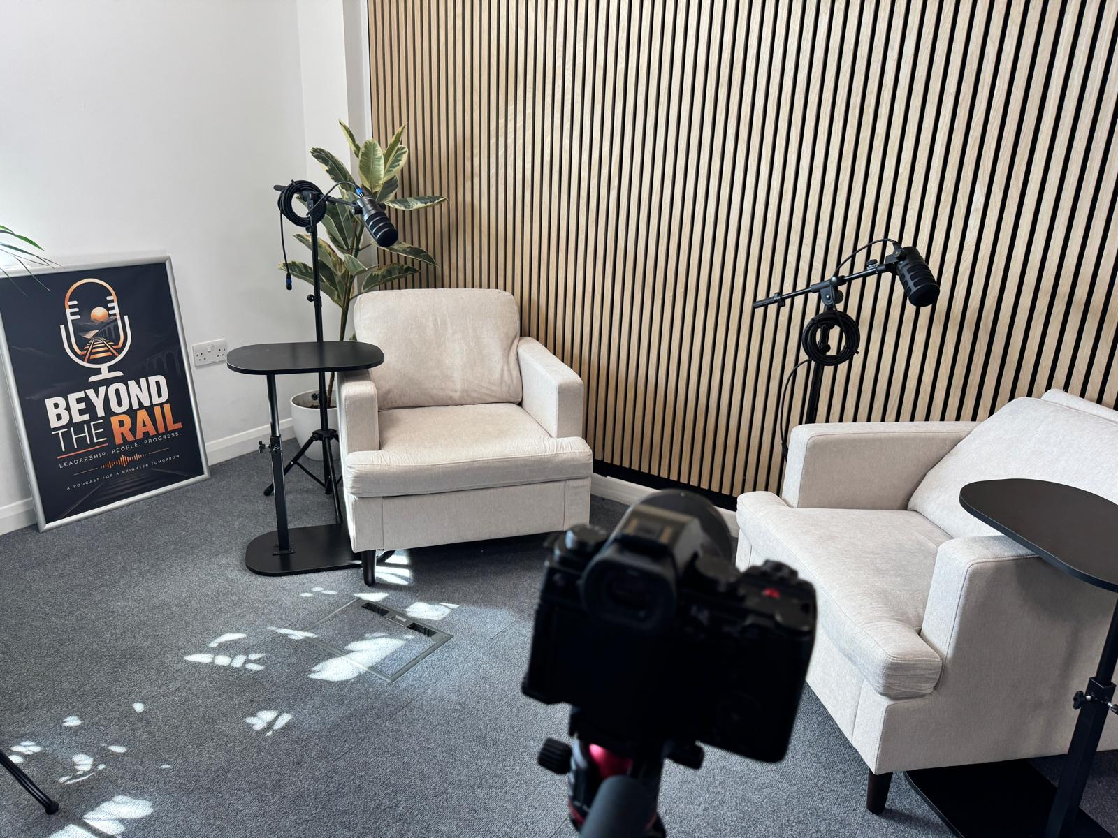 The finished podcast set with microphones, two cream chairs and the Beyond The Rail poster